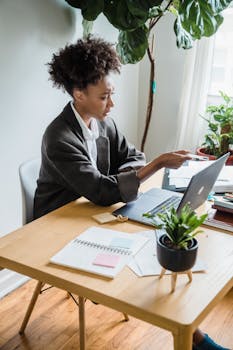 African American businesswoman engaged in remote work, using a laptop at a home office desk.