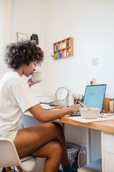A woman enjoying coffee while working on her laptop in a cozy home office.