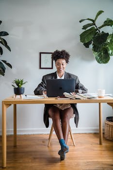 A woman working on a laptop in a stylish home office surrounded by plants, exuding productivity and modernity.