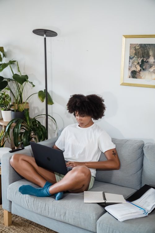Free Young woman working remotely from home, sitting cross-legged on a couch with a laptop. Stock Photo