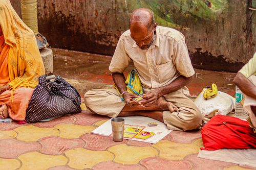 Free Elderly man sitting cross-legged on sidewalk, engaged in activity. Stock Photo