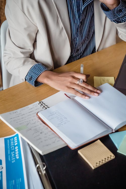 Free Woman Sitting Behind a Desk and Writing in a Notebook  Stock Photo