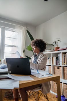 Woman working at a desk with laptop and papers, emphasizing remote work lifestyle.