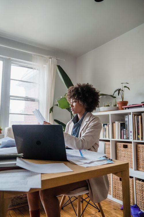 Free Woman working at a desk with laptop and papers, emphasizing remote work lifestyle. Stock Photo