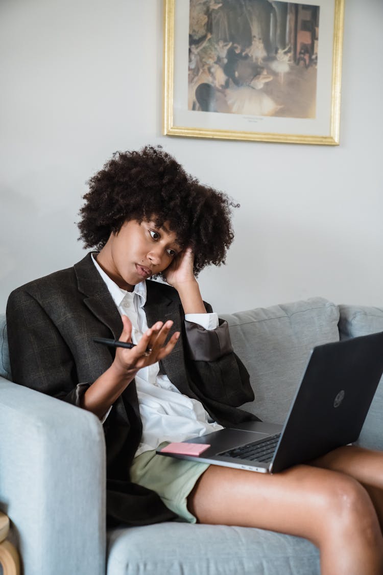 Woman Sitting On A Couch, Using Laptop And Looking Confused 