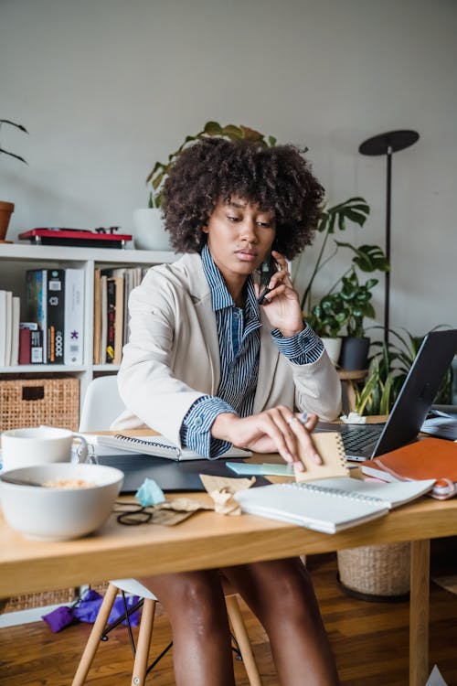 Free Woman Sitting in an Office, Looking Through Documents and Having a Phone Call  Stock Photo