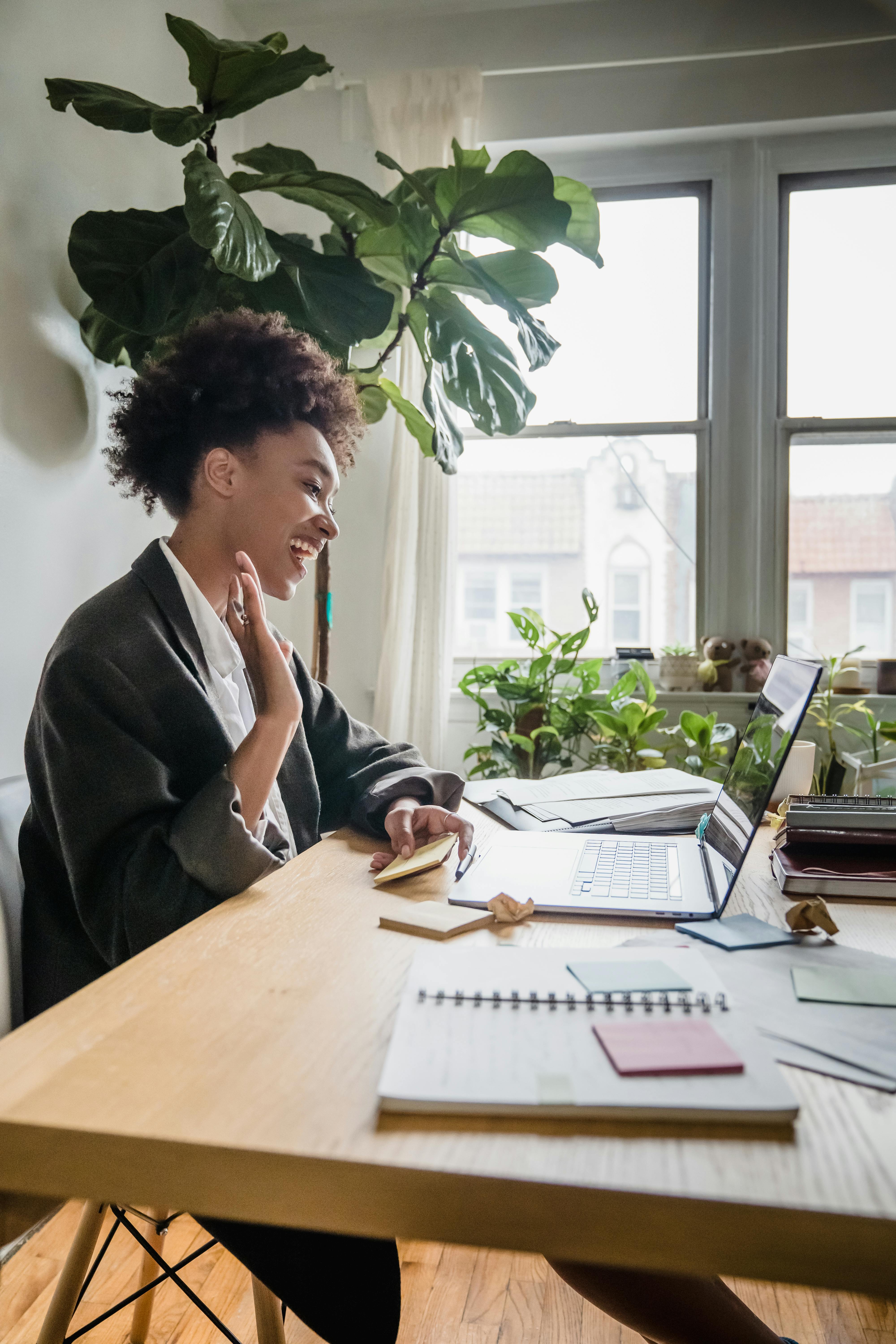 smiling woman sitting in an office and waving to a laptop screen