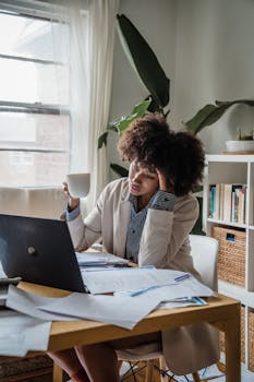 Woman in home office stressed while working remotely on laptop with coffee