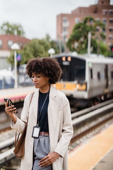 Young woman on train platform using smartphone, urban commute scene.