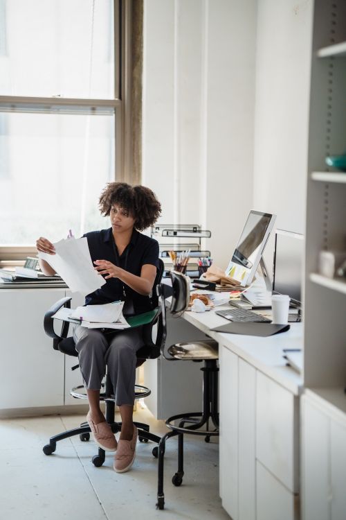 Free A woman reviewing documents at her office desk, showcasing a modern work environment. Stock Photo