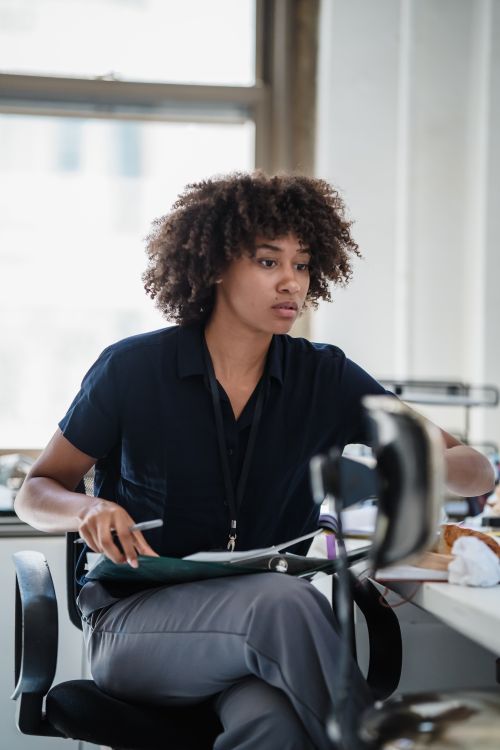 Free Focused woman in black shirt working at office desk with papers, showing determination and professionalism. Stock Photo