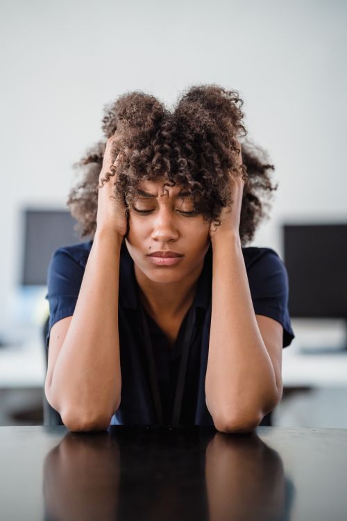 Caregiver Burnout Free Woman in office setting expresses stress, seated at desk with hands in hair. Perfect for workplace stress concept. Stock Photo