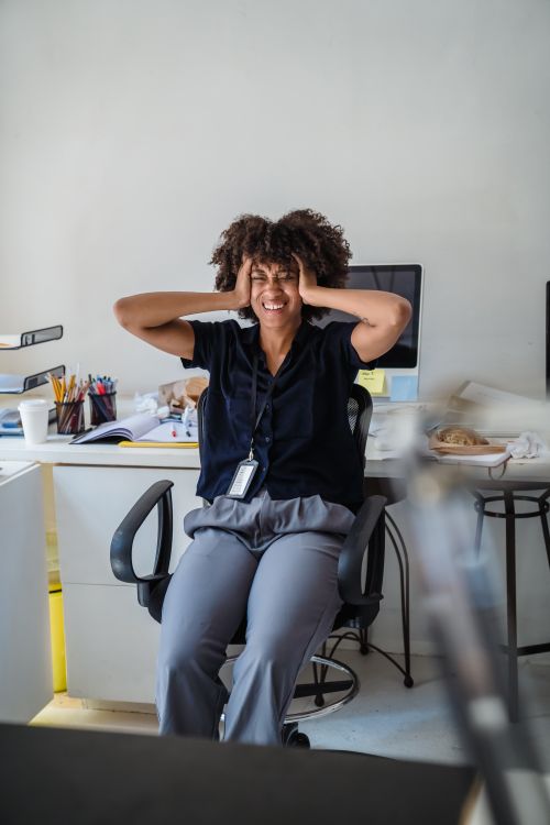 Free A woman in an office setting appears stressed, holding her head, surrounded by desk clutter. Business concept. Stock Photo