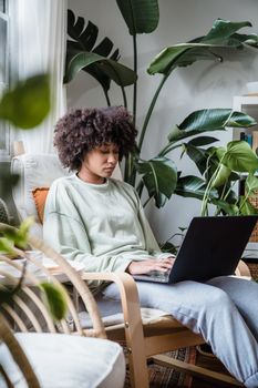 A woman sits working on her laptop in a cozy, plant-filled home office.