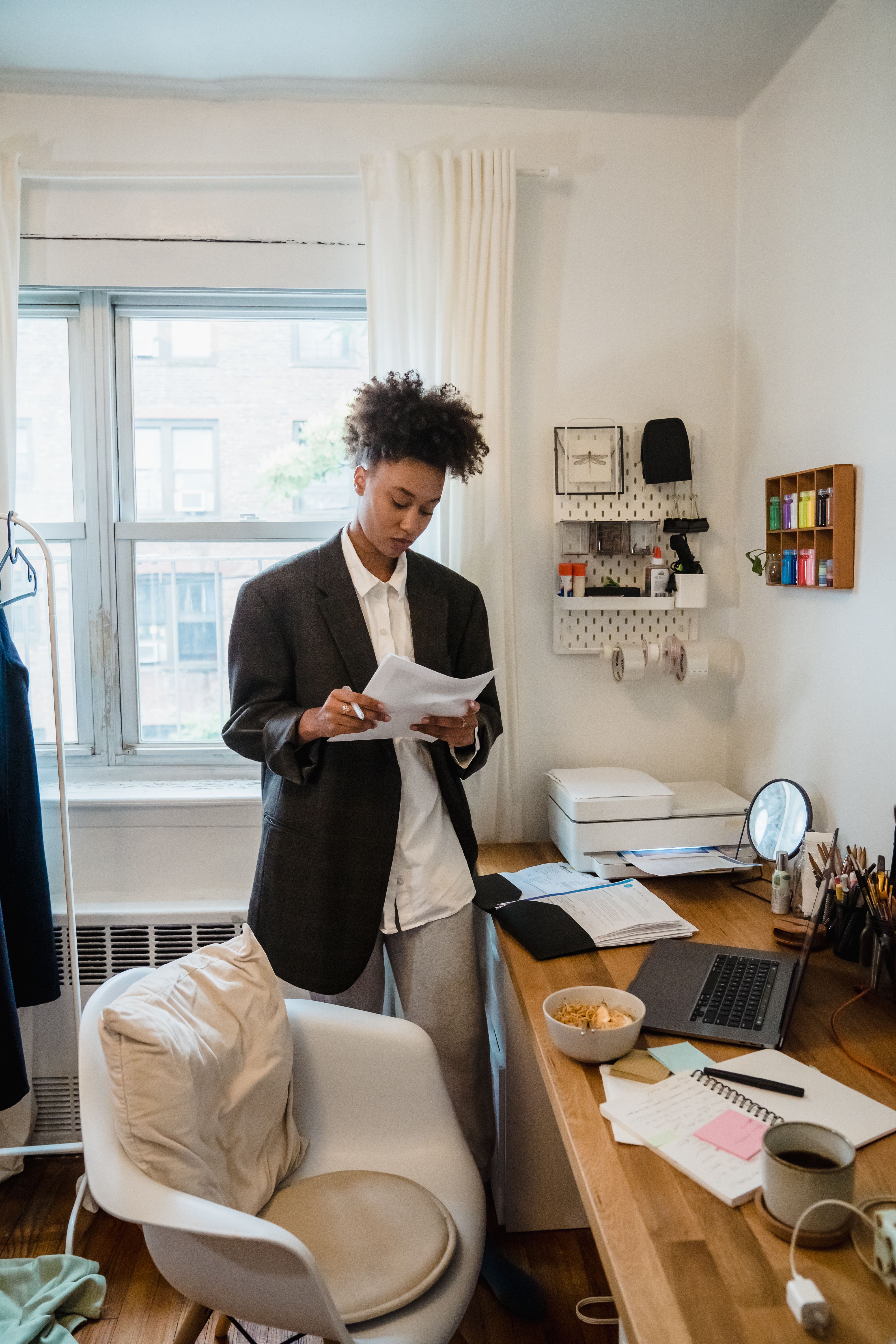 Woman in a home office setting reading documents with a laptop on the desk.