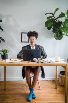 Woman working remotely in a stylish home office with lush plants and a laptop on a wooden desk.