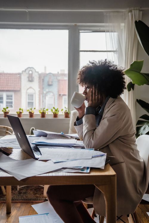 Free A woman sits at a cluttered desk drinking coffee while working from home. Stock Photo