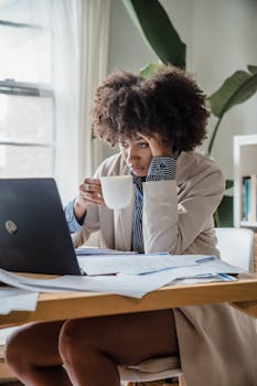 Woman working at desk with laptop and coffee cup, focusing on tasks.