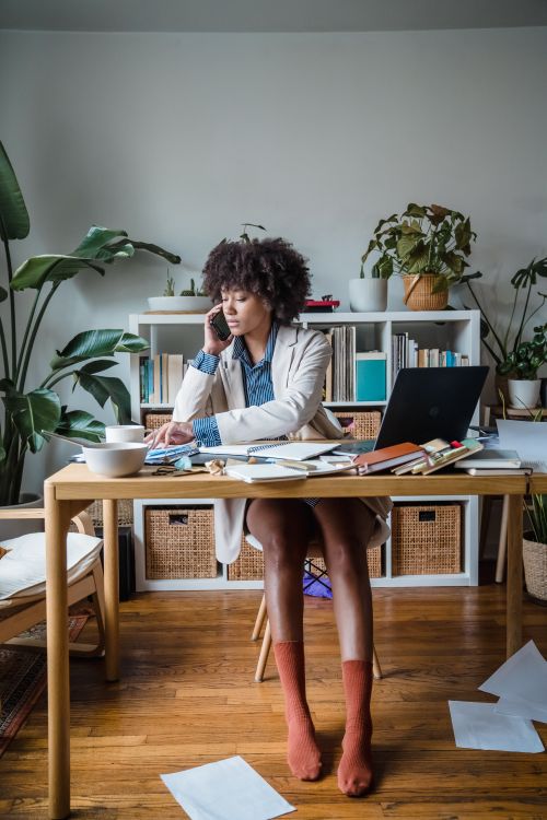 Free Adult woman multitasking in a home office amidst plants. Focused, stylish, remote work setup. Stock Photo