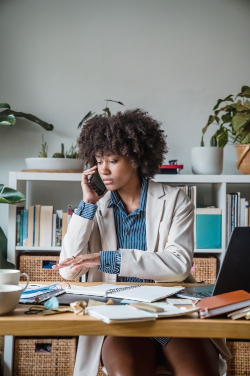 Free Professional woman multitasking with phone and documents in a modern home office setting. Stock Photo