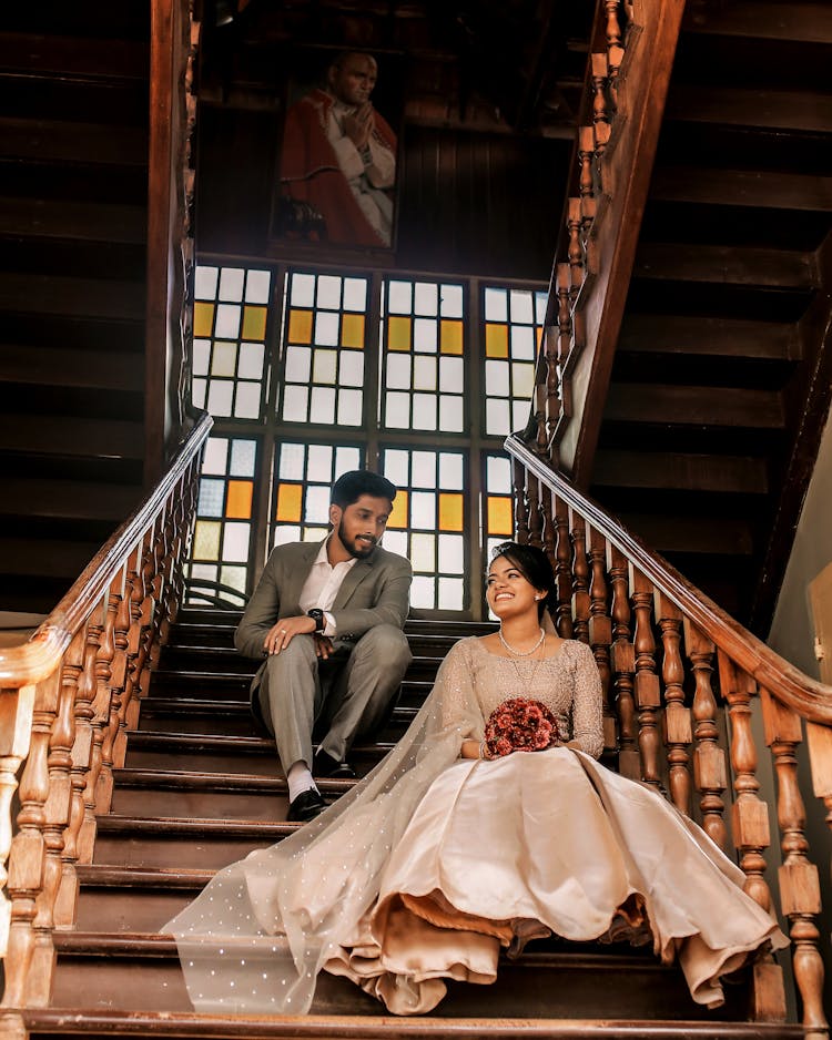 Low-Angle Shot Of A Romantic Wedding Couple Sitting On Wooden Stairs