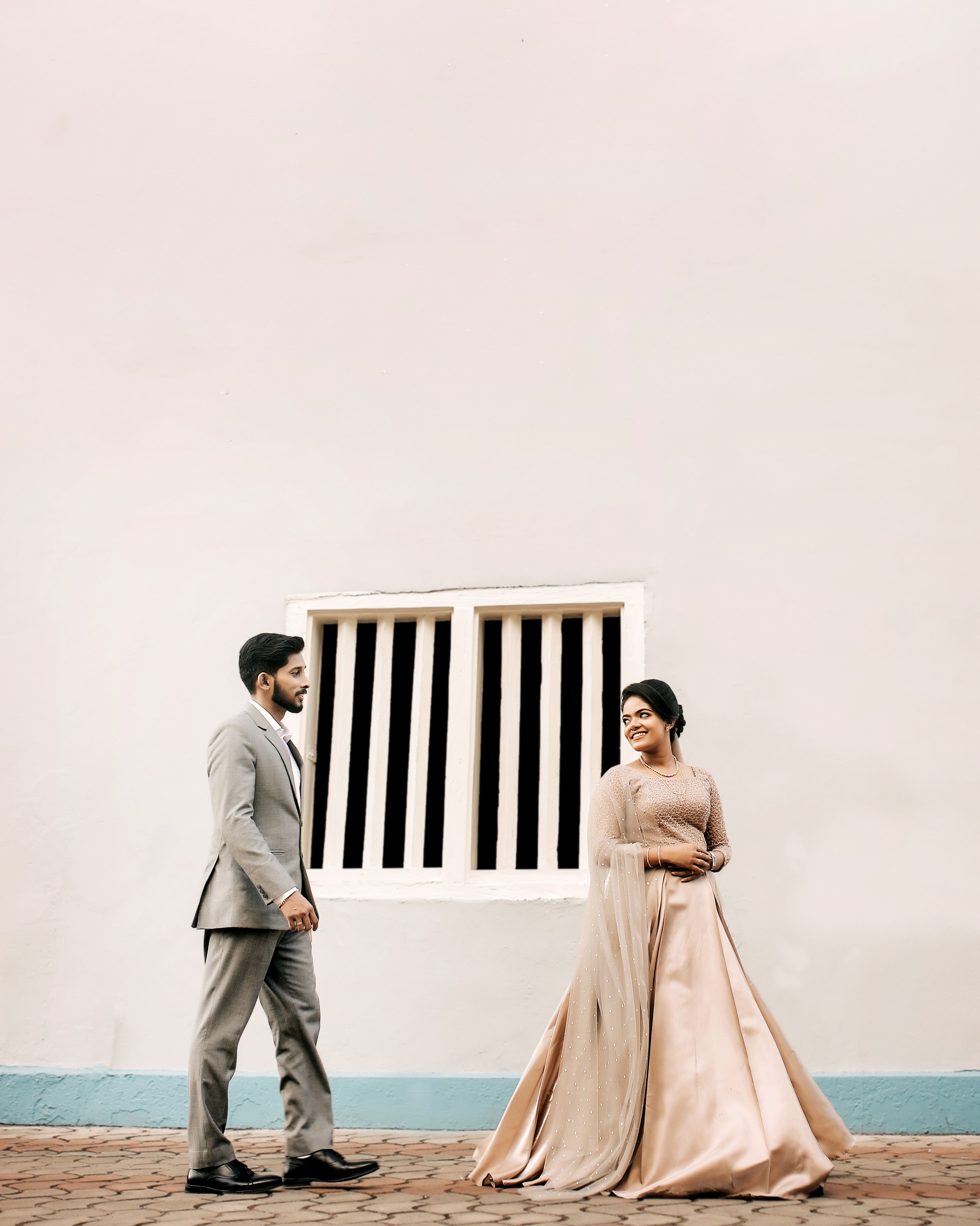 A stylish couple in formal attire during an engagement photoshoot with a minimalistic wall backdrop.