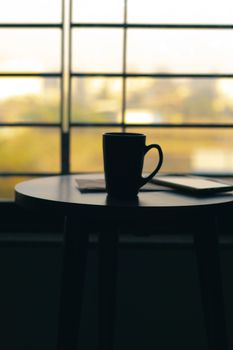 A black coffee mug placed on a table with morning sunlight streaming through a window, creating a cozy atmosphere.
