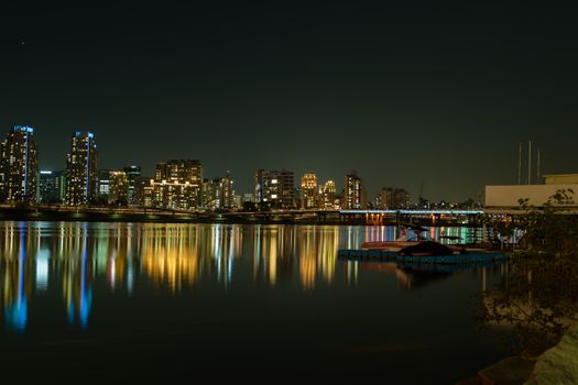 Night view of a city skyline with skyscrapers reflecting on a calm river, leaving a serene and vibrant impression.