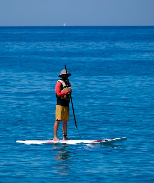 Woman in Red Tank Top and Black Shorts Standing on Surfboard on Sea