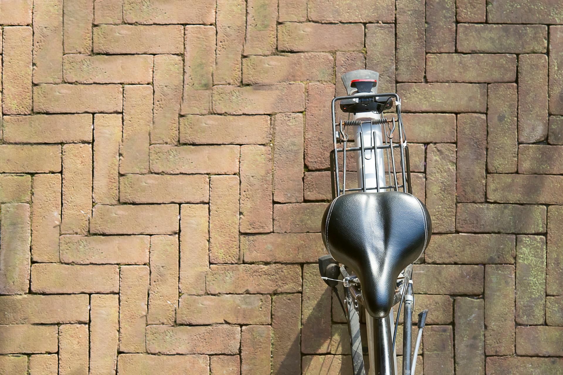 A bicycle saddle and rear rack on a herringbone brick pavement, viewed from above.