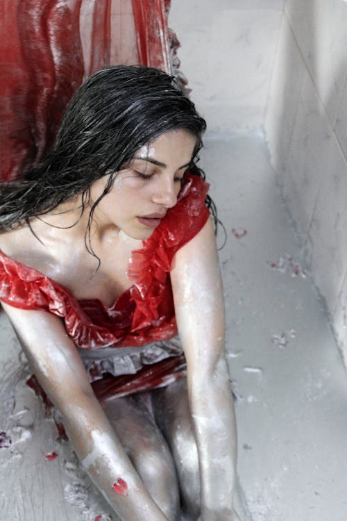 A Wet Woman in a Red Dress Sitting on a Floor with Silver Liquid