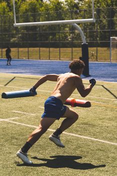 A shirtless man sprints on a grassy field during athletic training, demonstrating speed and strength.