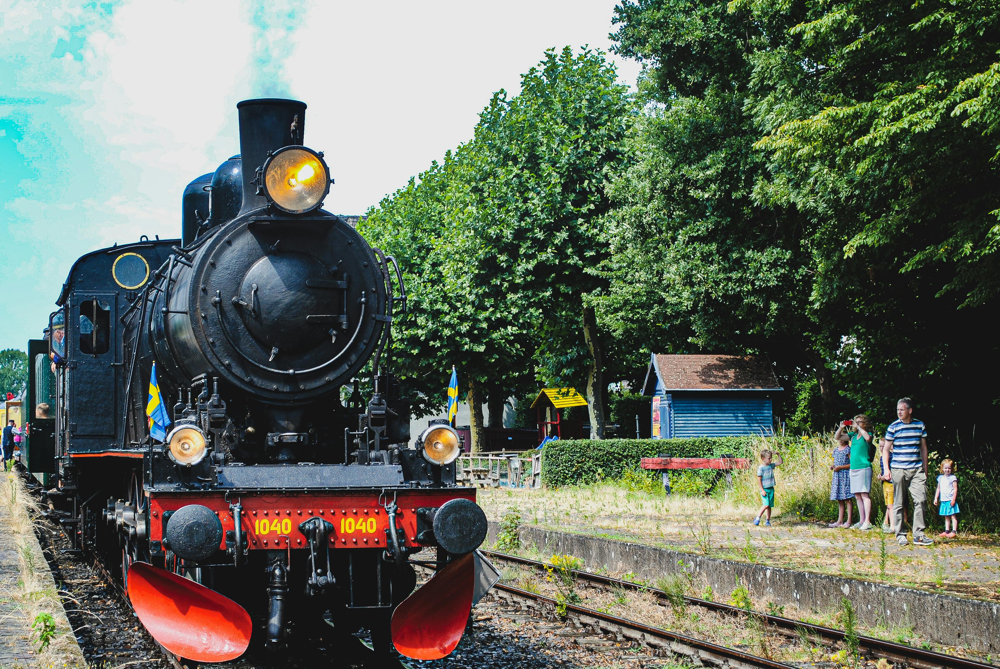 A vintage steam locomotive parked at a quaint railway station with spectators nearby.