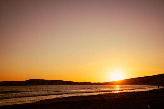 Golden sunset over the serene English bay with waves crashing and silhouettes on the shore.
