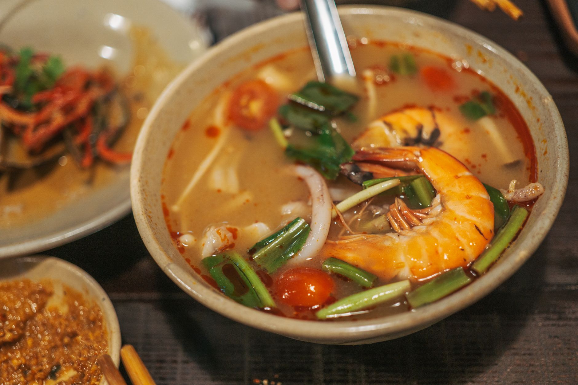 Steaming bowl of spicy tom yum soup with Thai chilies, lemongrass stalks, and fresh herbs floating on the surface