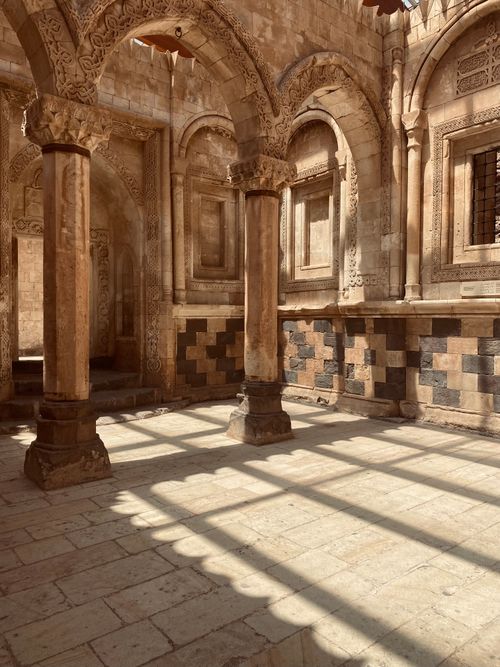 Free A sunlit courtyard featuring ancient stone columns and ornate carvings casting detailed shadows. Stock Photo