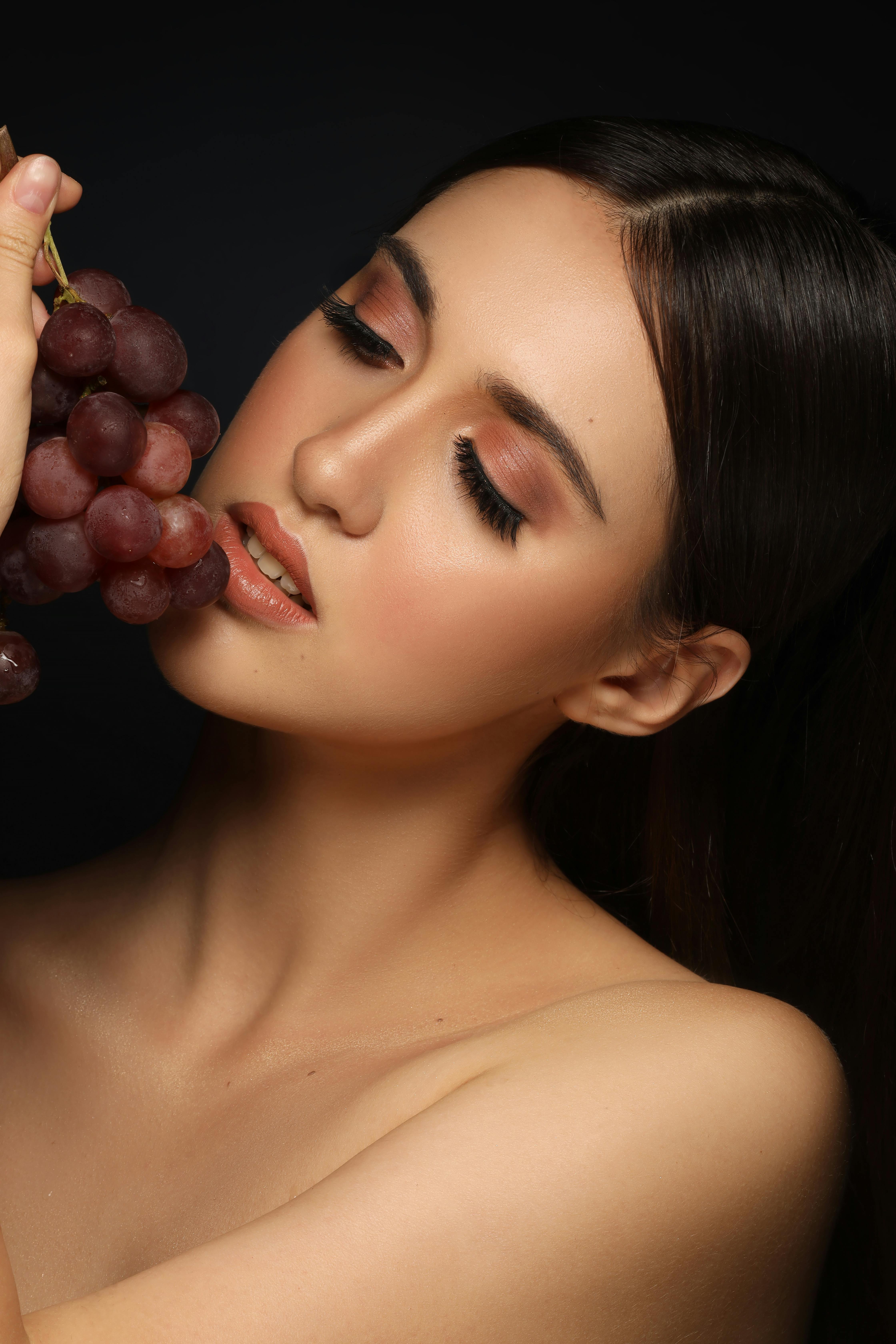 naked model with grapes on black background