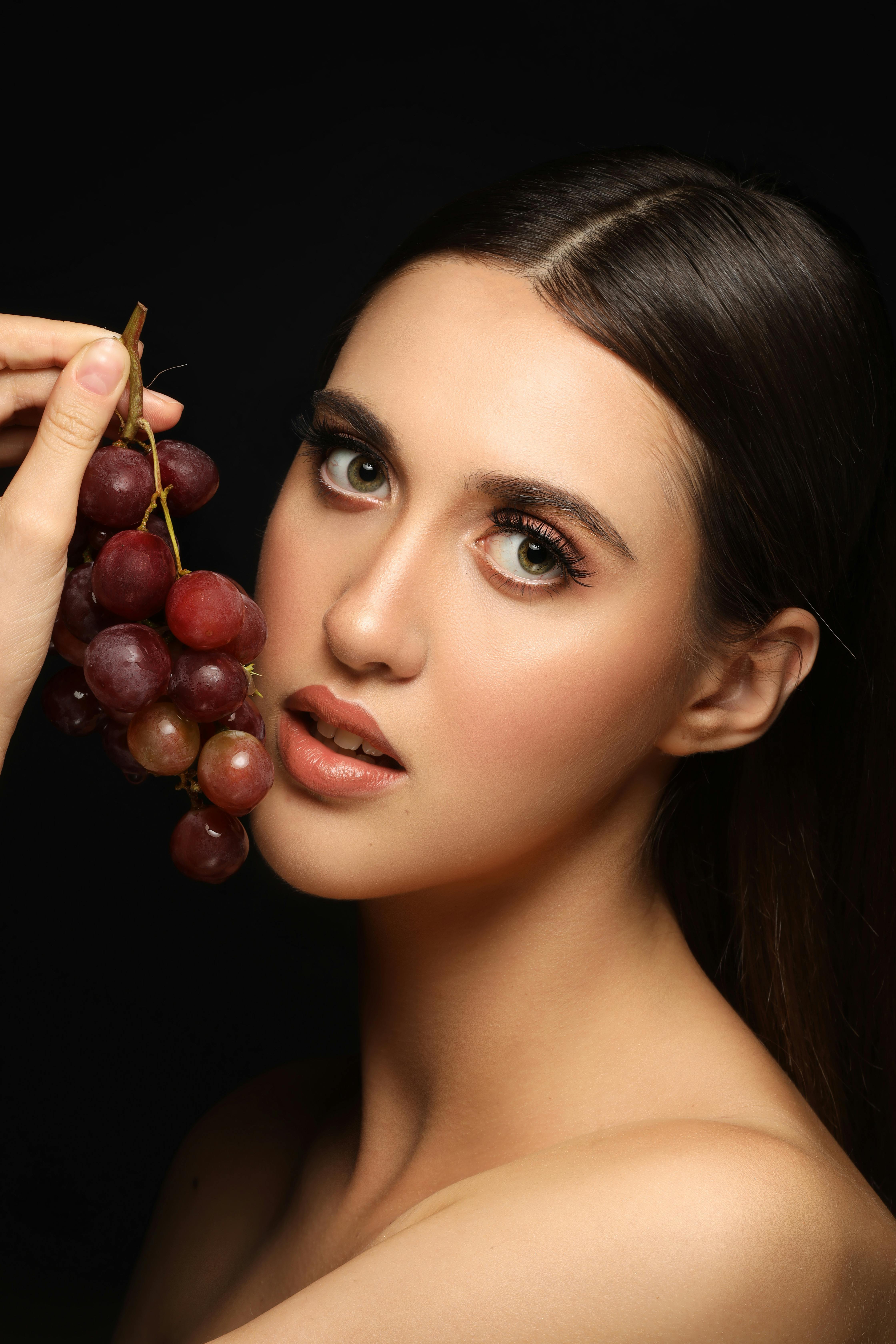 portrait of beautiful naked brunette with grapes on black background