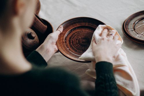Free A woman cleaning a wooden plate on a table with a towel in a cozy setting. Stock Photo