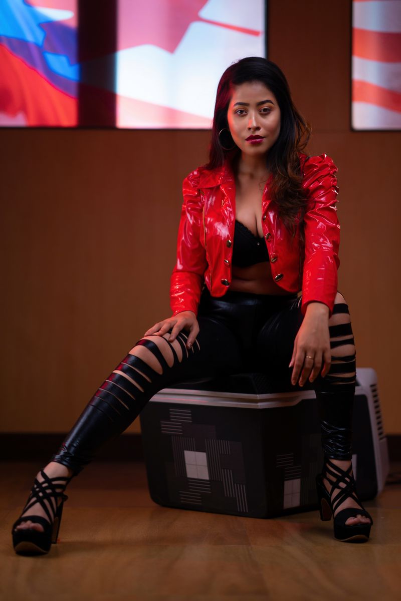 Fashionable woman in a red jacket poses indoors with a modern style and confident expression.