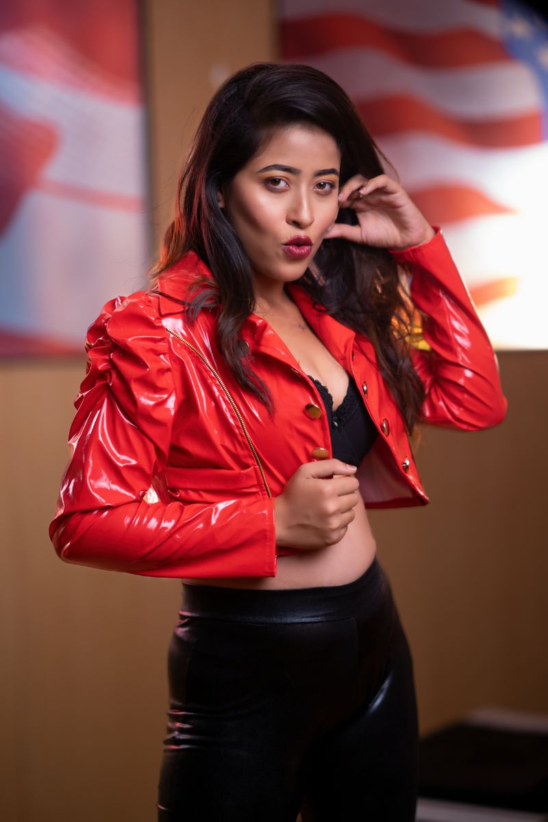 Fashionable woman striking a confident pose in red leather jacket and black pants indoors.
