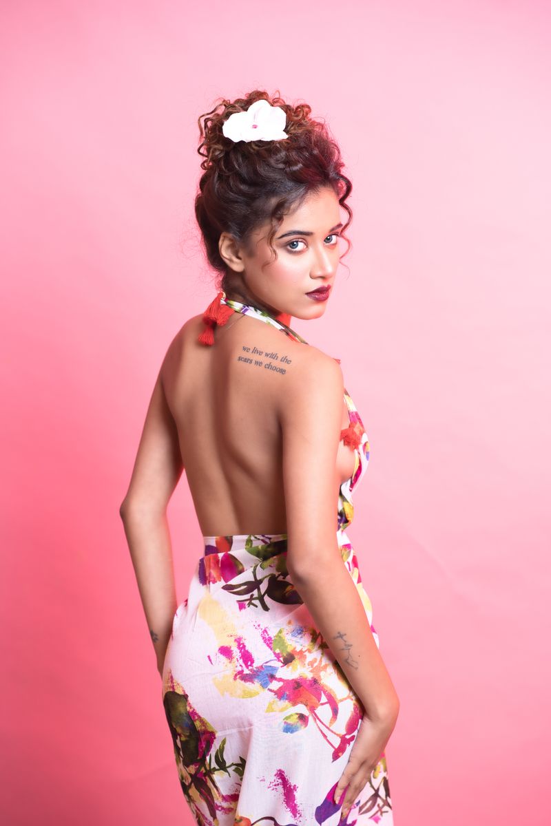 Stylish woman posing in a studio wearing a floral backless dress with a pink background.