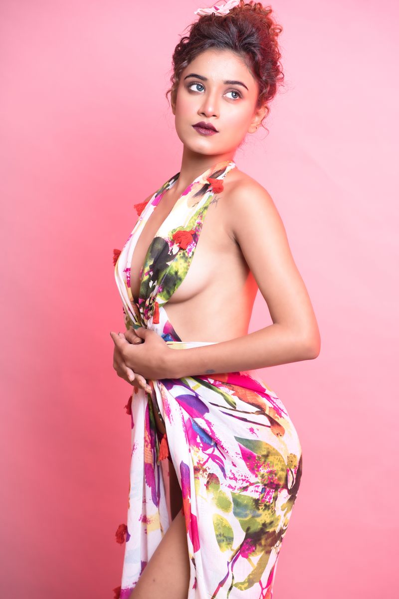 A stylish woman in a floral dress poses against a pink backdrop, combining elegance with modern fashion.