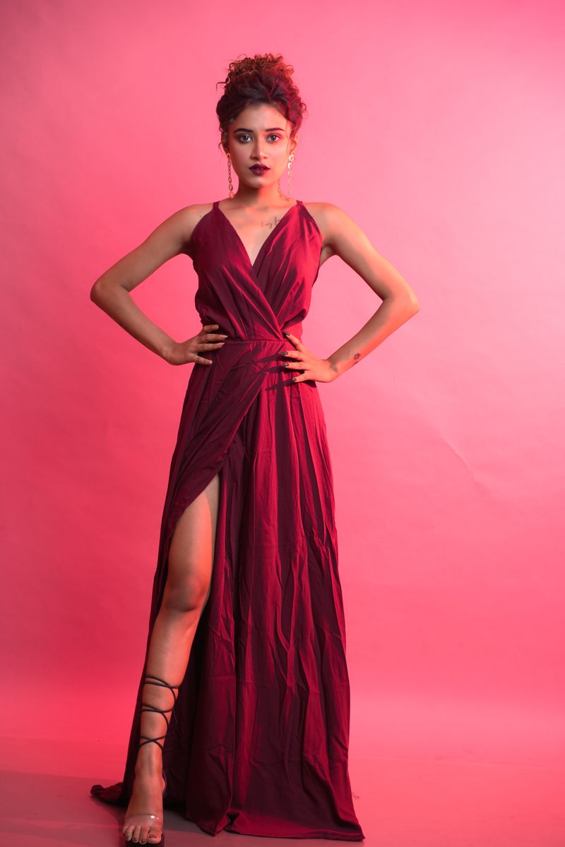 Stunning fashion portrait of a woman in a burgundy maxi dress with laced heels in a studio setting.