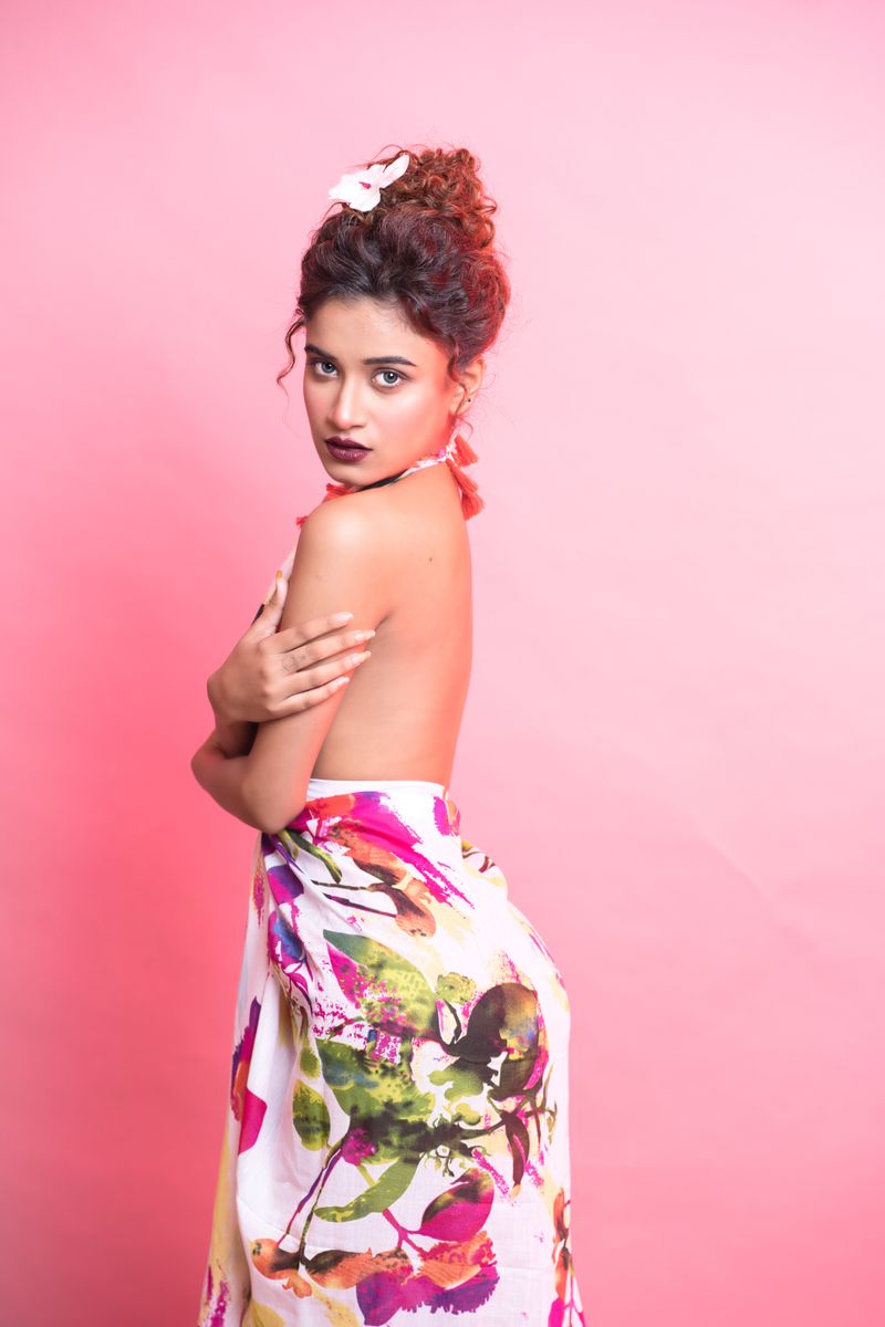 Beautiful woman wrapped in floral fabric against a pink background, exuding elegance and allure.