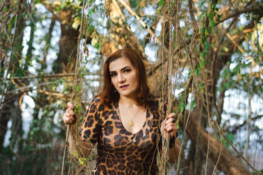 Woman in leopard print dress poses amidst vibrant tree branches in a serene outdoor setting.