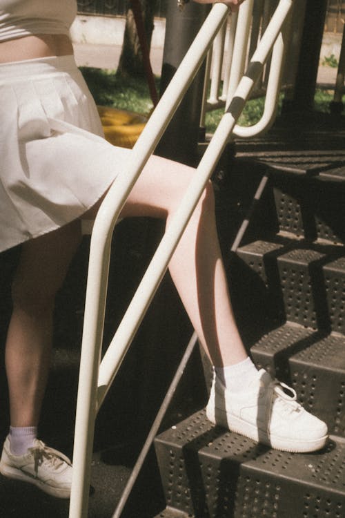 Person in White Shirt Standing on Metal Stairs with a Railing