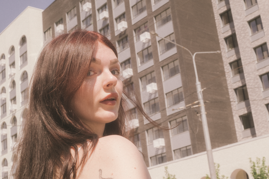 Close-up portrait of a brunette woman looking over her shoulder in an urban setting.