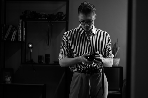 Free A fashionable man in glasses with a striped shirt adjusting a camera indoors. Stock Photo