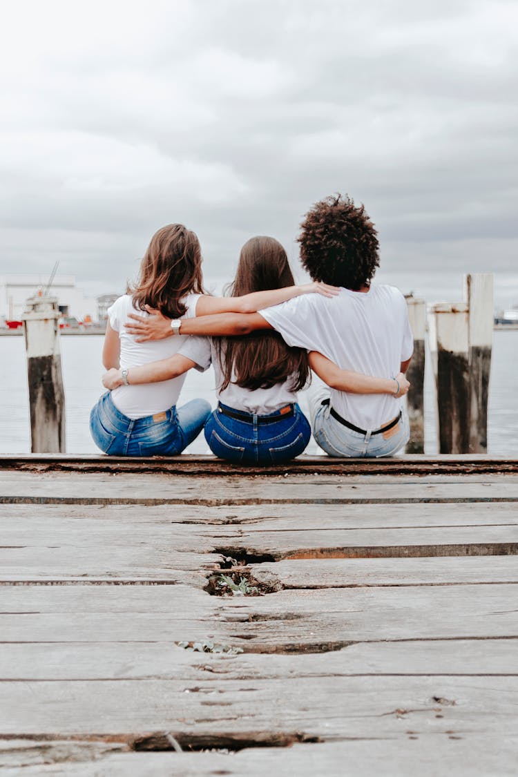 Friends Sitting On Pier Hugging